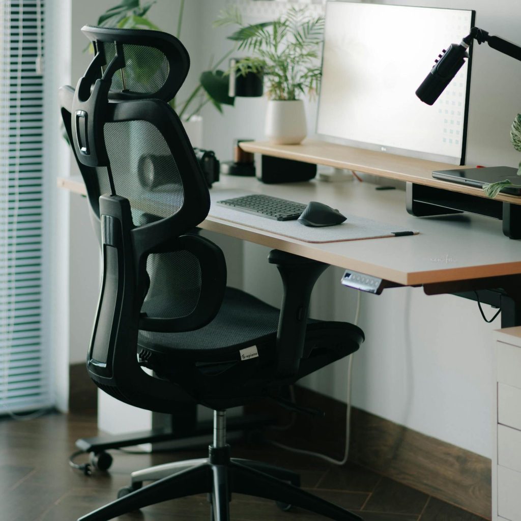 A sleek home office setup featuring a mesh ergonomic chair, desk, and greenery for a refreshing work environment.