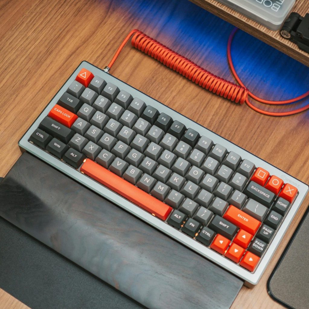 Modern mechanical keyboard with red accents on wooden desk, captured from above.